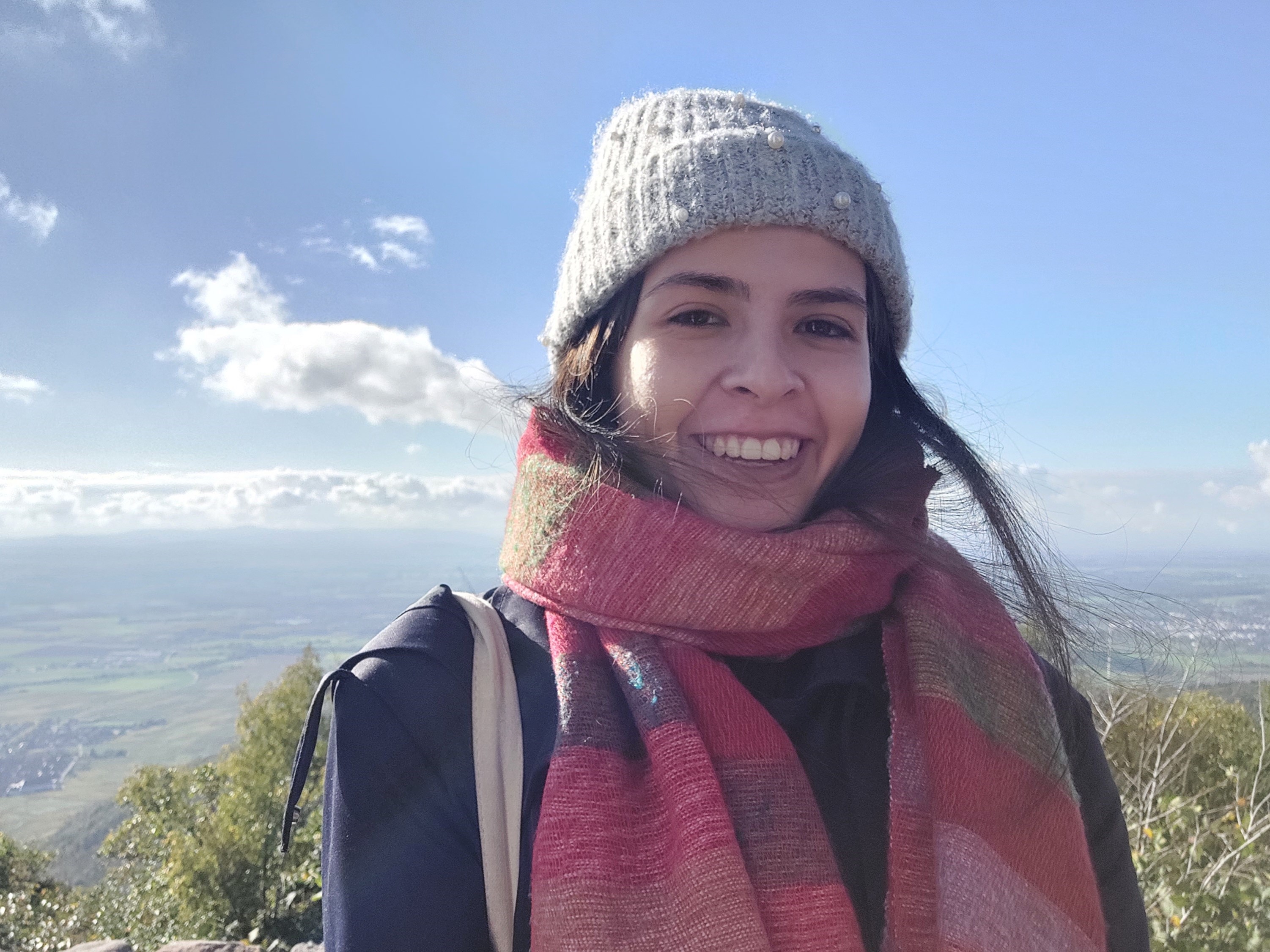 Nina Delvaux, a brunette wearing a grey beanie and a red scarf, with a view of the blue sky in the background